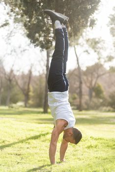 Man doing handstand on grass in the park. Athletic man wearing white tank top doing handstand in park.