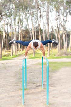 Male athlete exercising on parallel bars. Gymnastic man stand on bar and stretches his legs.