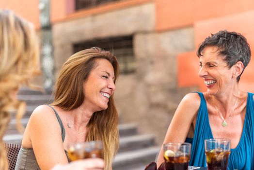 Middle-aged adult women enjoying drinks on an outdoor bar. Adult women laughing and having a good time.