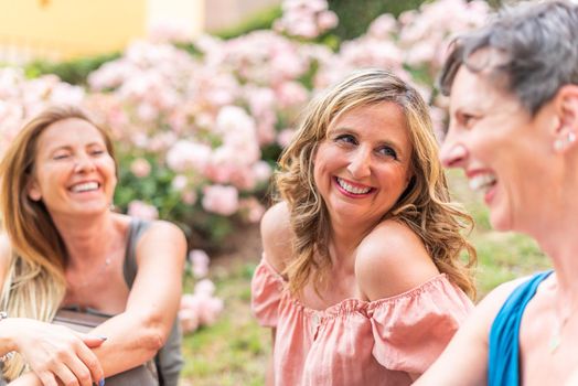 Three adult women sitting in the park laughing and chatting. Beautiful mature women having a good time together in the park.