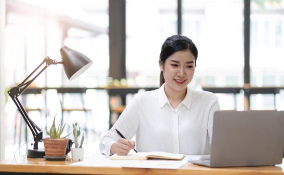 Beautiful young asian woman sitting at coffee shop using laptop. Happy young businesswoman sitting at table in cafe with tab top computer..