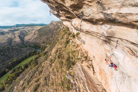 Aerial view of a rock climber holding on with one hand on rock. Climber with bare torso making an effort to climb the rock.