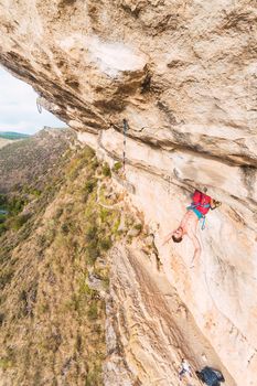 Aerial view of a climber clinging with his legs on the rock and belaying with the rope and making his body outward. Climber with bare torso climbing a rock wall.