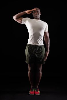 African american man greeting at camera with a military salute in an act of honor and patriotism, showing respect. Athlete adult man standing wearing sportswear on a black background.