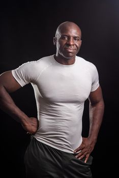 Portrait of an african american man standing looking at camera with hands on waist. Muscular adult male in sportswear in a studio with black background.