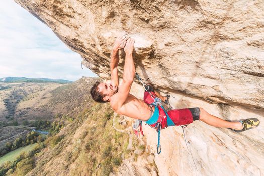 Climber grimacing as he holds on with both hands on the rock. Climber with bare torso making an effort to climb the rock.