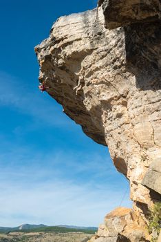 Distant view of a rock climber hanging and climber a rock formation with a blue sky background.. Vertical view of a bare torso climber climbing a rock.