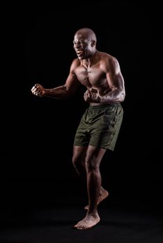 Side view of an african american man with fists clenched and shouting on a black background. Athletic adult man standing dressed only in shorts with a black background.