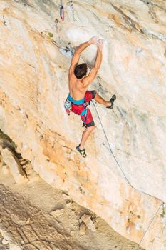 Aerial view from above of the back of a man climbing a rock formation. Man with bare torso climbing a rock wall.