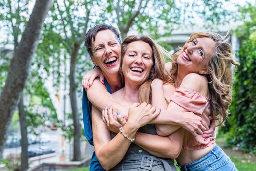 Close up of three cheerful mature female friends hugging together. Middle aged friends sharing time together and having fun.