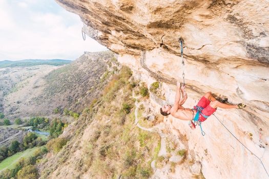 Aerial view of a rock climber hanging on with his two hands in a rock formation. Climber with bare torso climbing a rock wall.