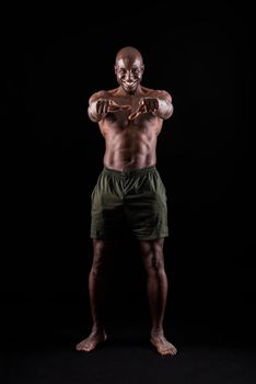 African american muscular man smiling standing and pointing at camera with both hands on a black background. Bodybuilder with bare torso wearing shorts in studio.