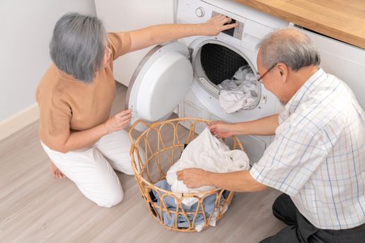 Senior couple working together to complete their household chores at the washing machine in a happy and contented manner. Husband and wife doing the usual tasks in the house.