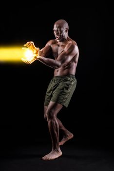 African American man doing a performance of a famous Japanese cartoon character performing a power throw. Muscular man with black background standing dressed only in shorts.