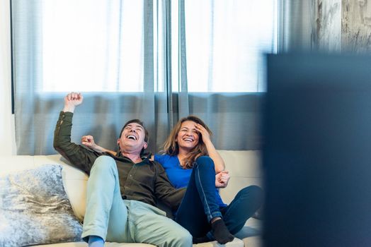 Mature couple celebrating something they are watching on TV. High quality photo