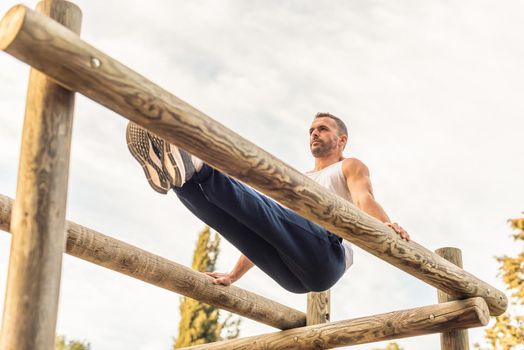 Male athlete exercising on a wooden structure. Male gymnast standing with both arms on wooden bars, lifting his body and making his legs straight forward.