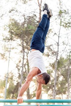 Man doing handstand on bars in the park. Athletic man wearing white tank top doing handstand in park.