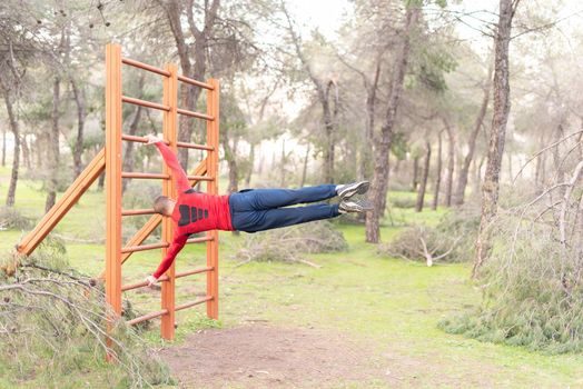 Rear view of a young man doing exercises on vertical bar in park. Gymnastic man performing human flag figure on bars in a park.