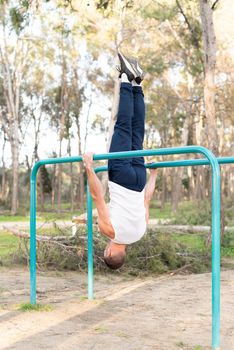 Male athlete exercising head to the ground on parallel bars. Male gymnast holding himself upside down on bars.