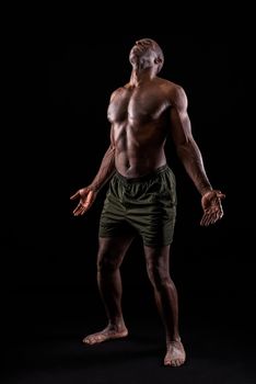 African American man with hands open and head bent backwards. Muscular man with black background standing wearing shorts on a black background.