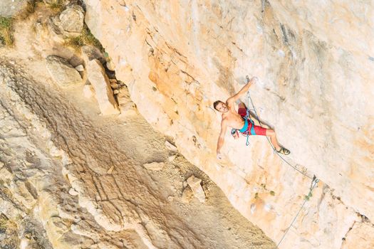 Distant view of a rock climber in the middle of a rock formation. View from above of a rock climber hanging in the middle of the rock formation and looking at camera.