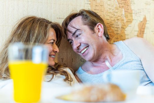 Mature couple laughing in bed, holding a tray with breakfast. High quality photo