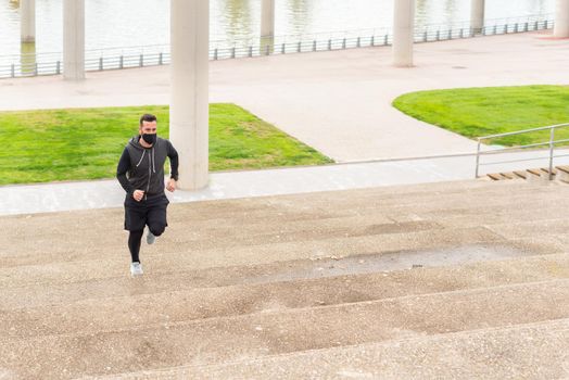 Runner climbing the stairs. Young athlete dressed in sportswear wearing a mask while jogging. High quality photo