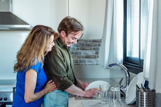 Man washing the dishes with his wife next to him. High quality photo