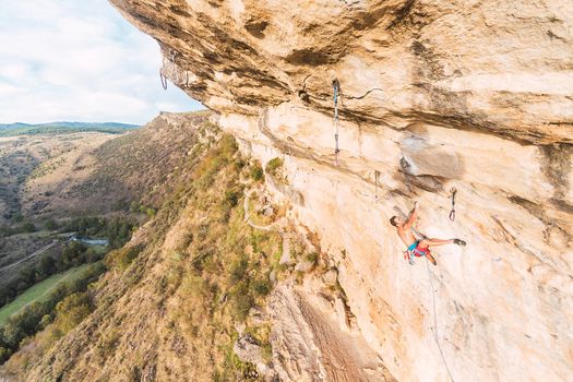 Aerial view of a rock climber climbing a rock formation. Climber with bare torso climbing a rock wall.