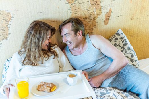 Mature couple laughing in bed, holding a tray with breakfast. High quality photo