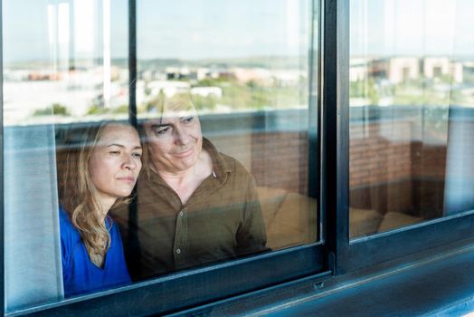 Mature couple looking sad out the window from home. High quality photo