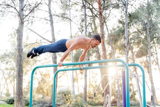 Side view of a male athlete exercising on parallel bars. Gymnastic man stand on bar and stretches his legs together.