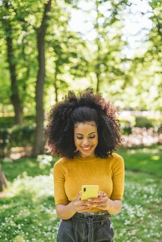 Pretty afro woman typing on mobile, in the forest. Selective focus.