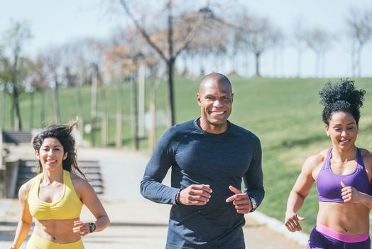 Two women and a man with a mask running in a park. Front view.