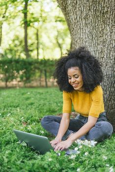 Beautiful and happy afro woman typing on a laptop in a garden. Selective focus.