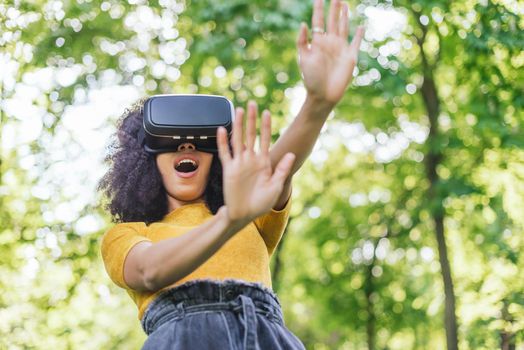 Afro woman wearing a virtual reality glasses in a garden. Selective focus.