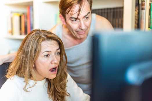 Middle-aged couple looking surprised at computer at home. High quality photo