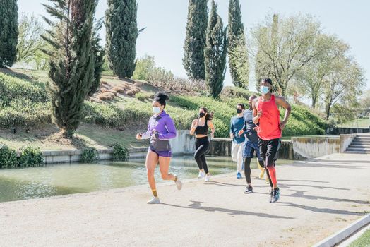 Group of six runners with mask training in a park. Full body.