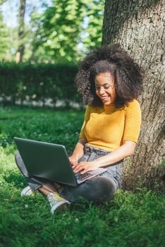 Beautiful and happy afro woman typing on a laptop in a garden. Selective focus.