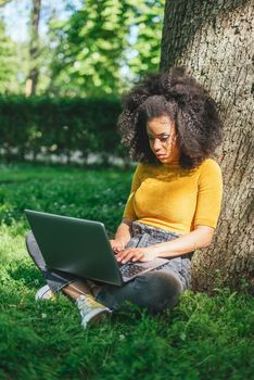 Beautiful afro woman typing on a laptop in a garden. Selective focus.