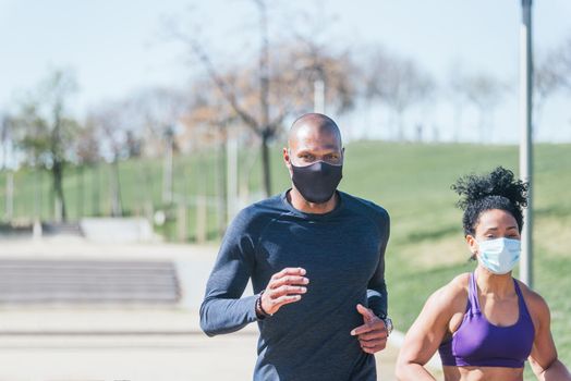Man and woman with mask running in a park. Front view.
