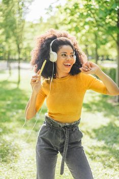 Pretty afro woman listens to music with headphones dancing in a garden. Selective focus.