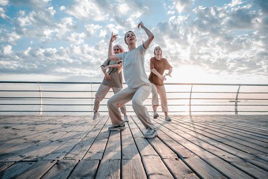 Young dancing teenager girls enjoying funky hip-hop moves. Modern women performing freestyle dance together on sea embankment at sunrise. High quality photo