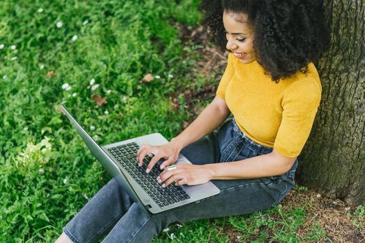 Beautiful and happy afro woman typing on a laptop in a garden. Selective focus.