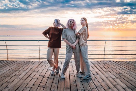 Dancing group of young talented freak women performing freestyle hip-hop moves. females enjoying modern dance expression. Outdoor training near sea or ocean during sunset. High quality photo