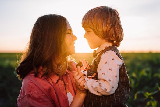 Tender scene of loving son with mom on sunset backdrop. Beautiful family. Cute 3 year old kid with mother. Parenthood, childhood, happiness, children wellbeing concept. High quality photo
