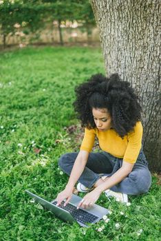 Beautiful afro woman typing on a laptop in a garden. Selective focus.