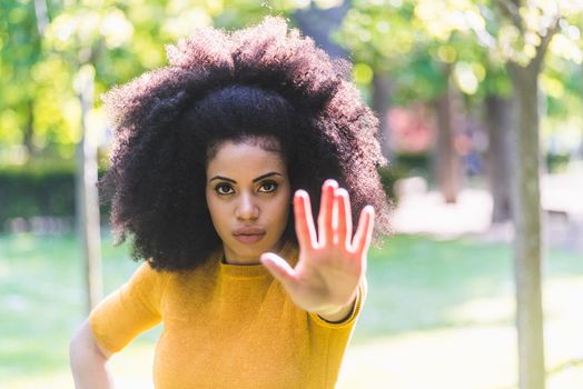 Portrait of pretty afro girl in a garden saying stop with her hand. Selective focus.