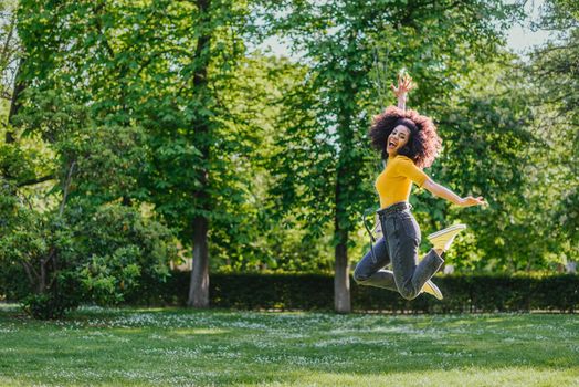 Pretty woman jumping happily in a garden. Side view. Full body.