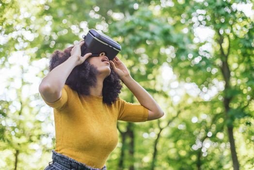 Afro woman wearing a virtual reality glasses in a garden. Selective focus.